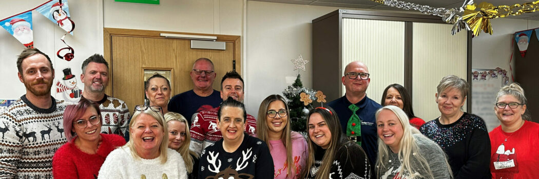 The staff at Hodge Clemco wearing their Christmas Jumpers stood round the Christmas tree.
